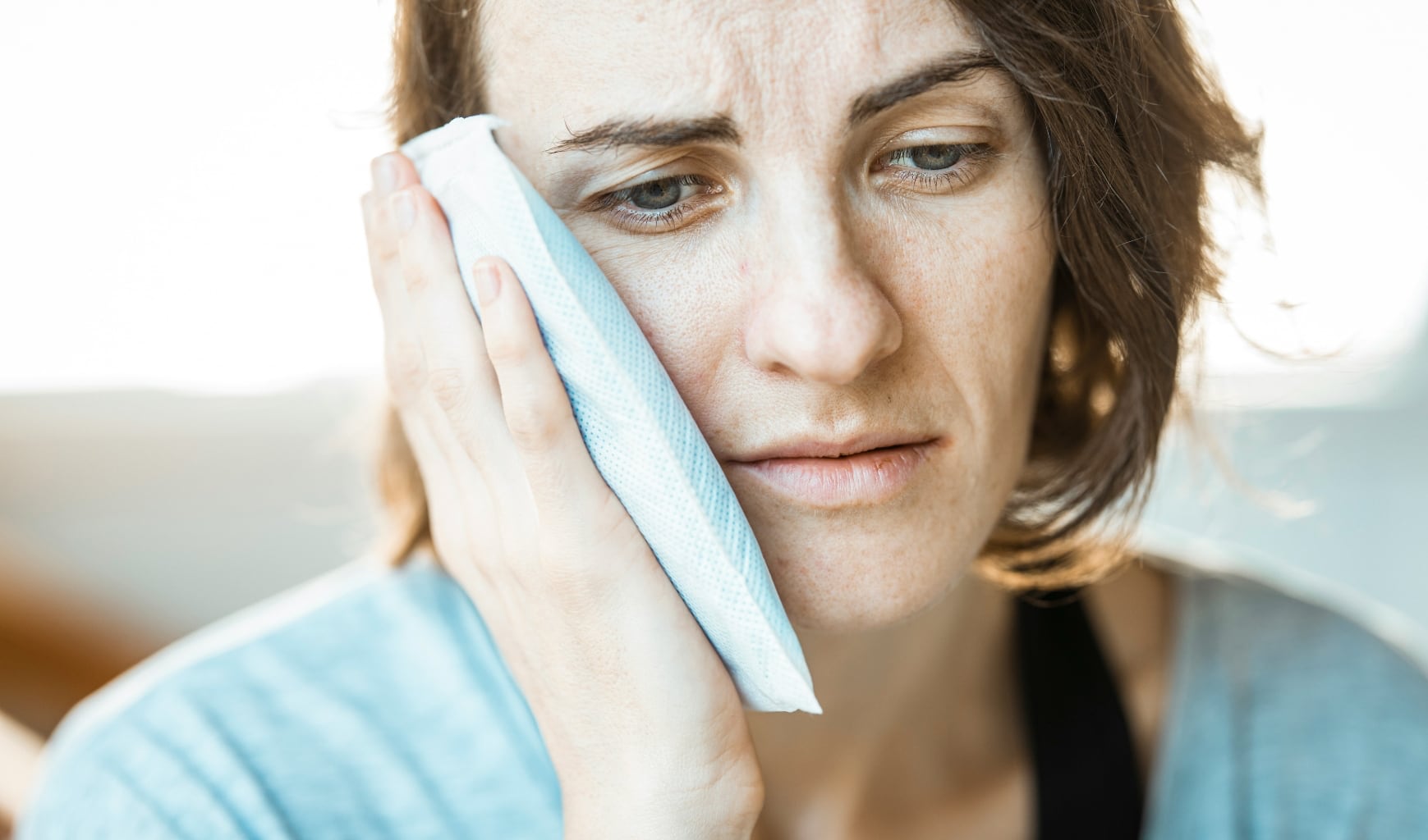 Ein Symbolbild für eine Frau die sich mit einem Kühlpack ihre schmerzende Wange kühlt